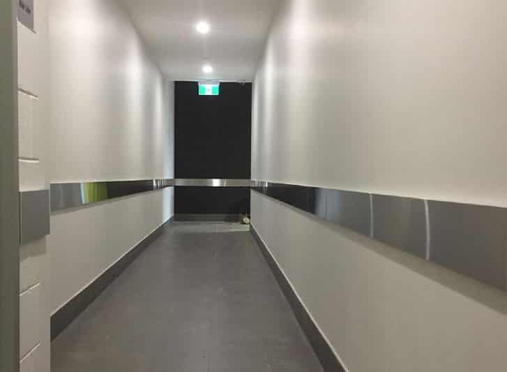 A hallway with a white wall and stainless steel railings.