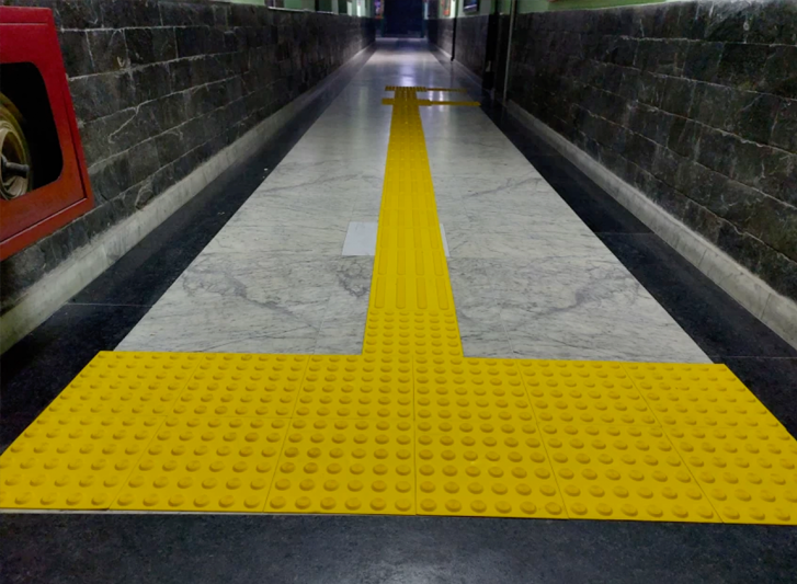 A yellow tiled walkway adorned with stainless steel studs and tactile tiles in a subway station.