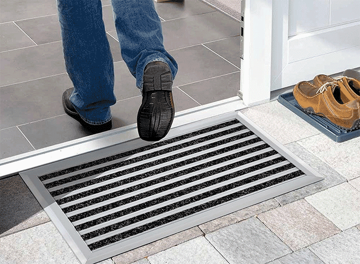 A man is standing in front of a door with a doormat made of aluminium.