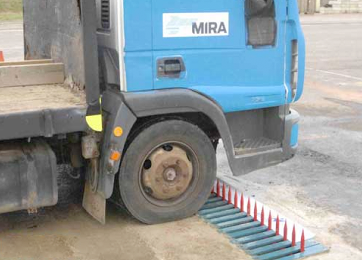 A blue truck is parked next to a concrete barrier with stainless steel crash bollards.